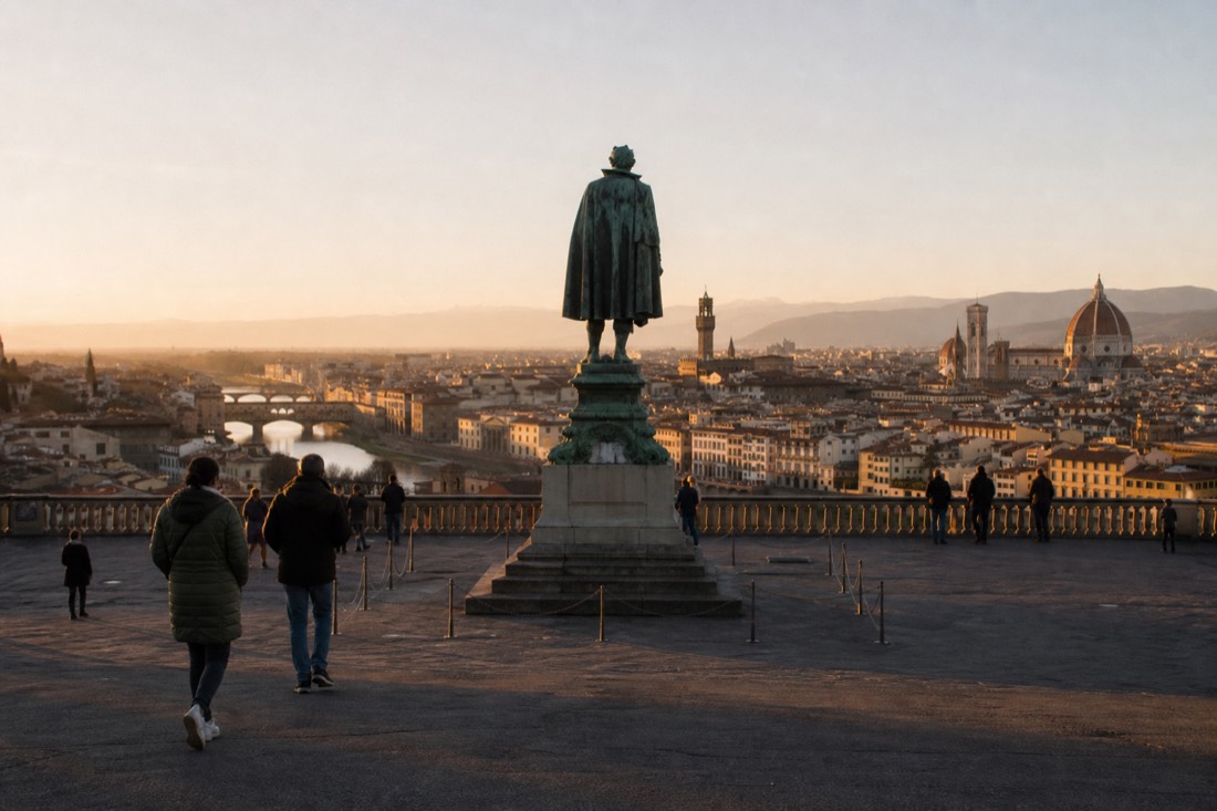A dark green bronze statue on a stone plinth at the center of a panoramic terrace overlooking Florence and the Arno at dusk
