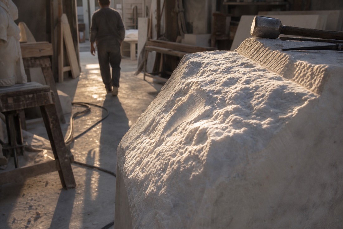 Close view of white Carrara marble with chisel marks and drill grooves caught in raking light inside a Florentine sculpture workshop