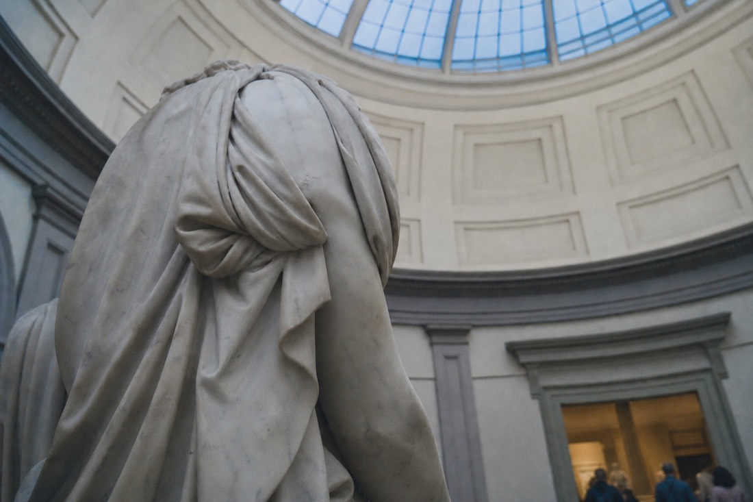 Low upward view of the marble David's torso and shoulders against the pale coffered dome of the Tribuna ceiling in the Accademia Gallery