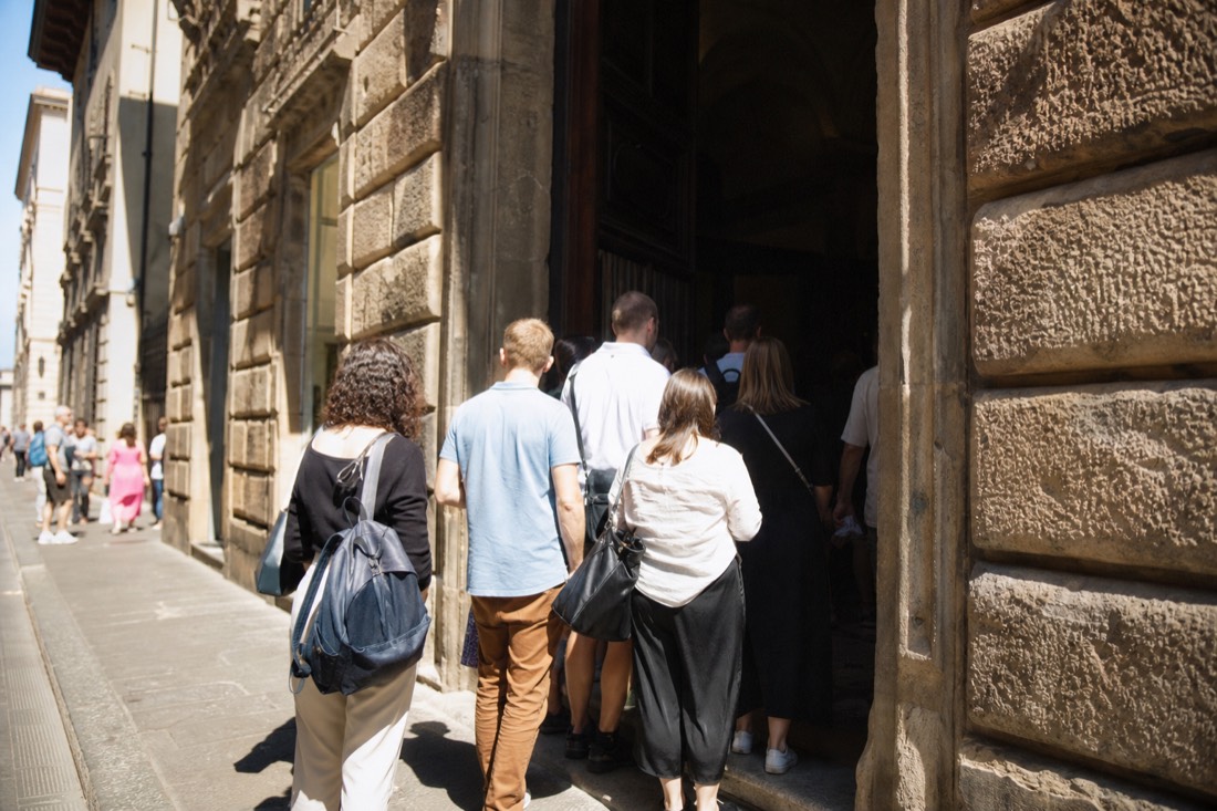 Morning light on the entrance of the Accademia Gallery on Via Ricasoli with a short line of visitors under the stone doorway