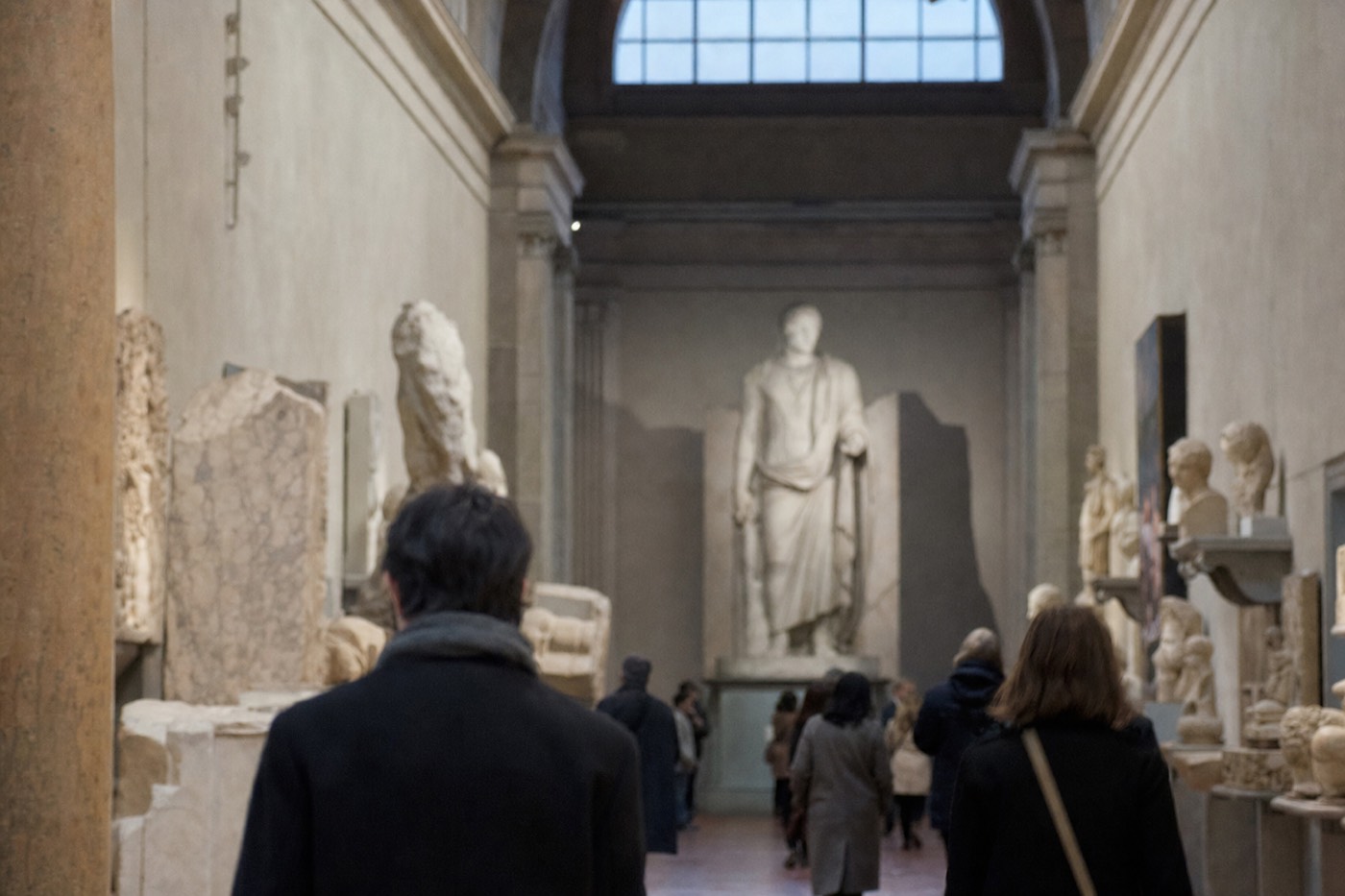 Visitors standing in the domed Tribuna of the Accademia Gallery in Florence looking up toward a tall marble figure on its pedestal