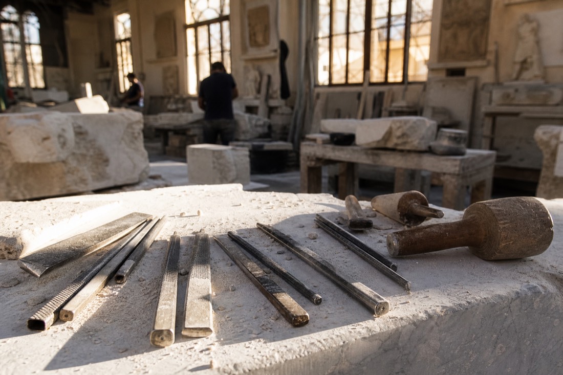 Sculptor's chisels, rasps and a wooden mallet resting on a marble workbench dusted with fine white powder