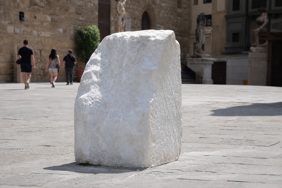 Weathered block of raw white marble standing in a Florence stone courtyard with morning light raking across its surface