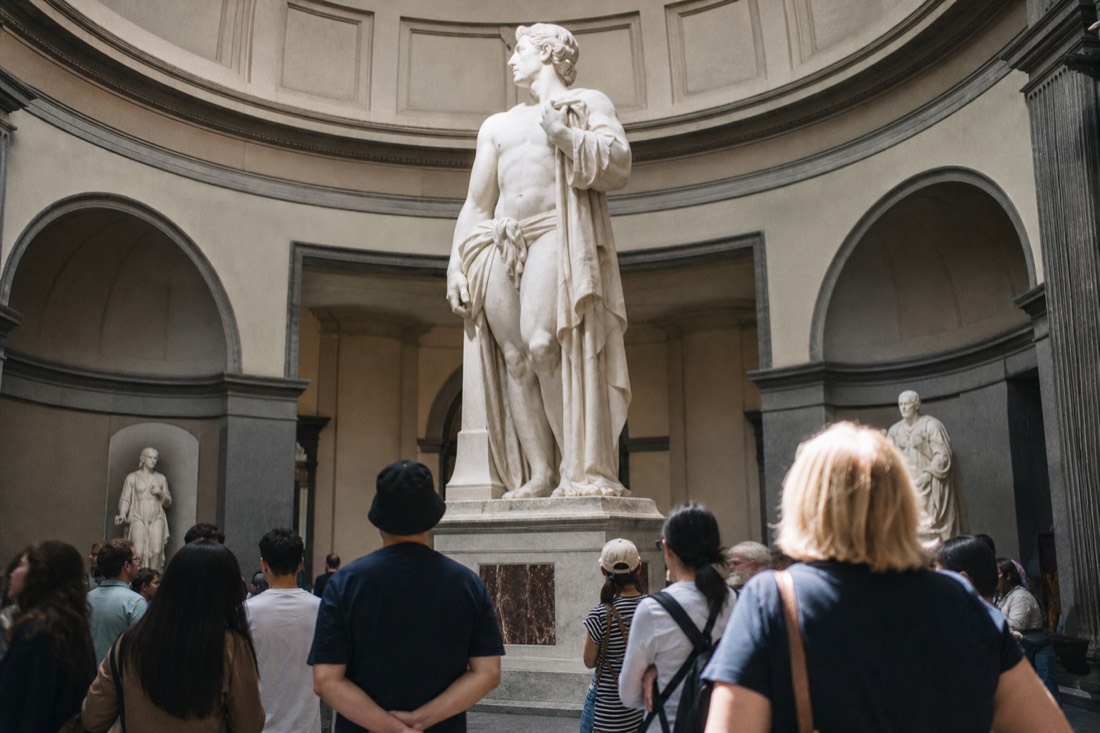 Visitors gathered in a semicircle around the base of the marble David beneath the skylight of the Accademia Tribune in Florence