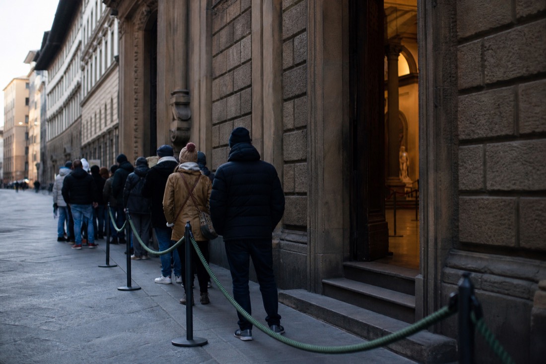 A short reserved-entry line beside rope barriers at the Accademia Gallery entrance on Via Ricasoli in morning light