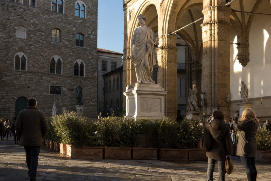 The marble replica David standing in Piazza della Signoria beside the stone arches of the Loggia dei Lanzi in Florence