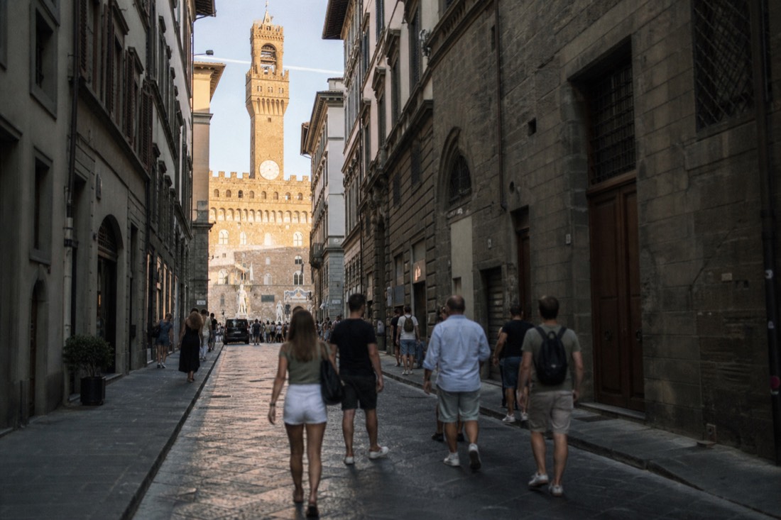 A cobbled Florence street leading from Via Ricasoli toward Piazza della Signoria in warm afternoon light with the Palazzo Vecchio tower ahead