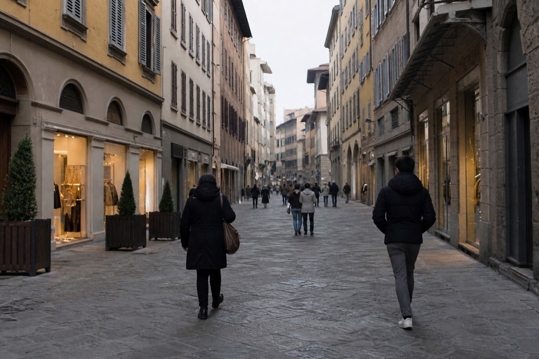Wide pedestrian shopping street in central Florence with stone paving and shuttered upper windows in early morning