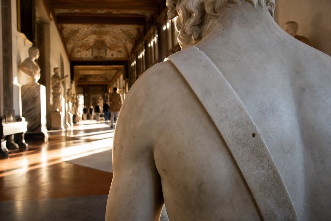 Close view of the marble sling strap running across the shoulder and back of a monumental statue under raking gallery light