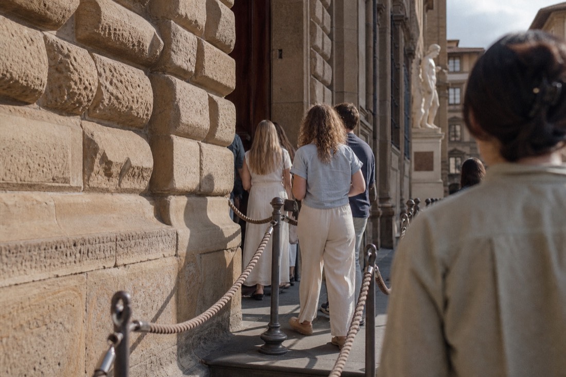 A short morning queue beside the entrance of the Accademia Gallery on Via Ricasoli with rope barriers and soft shadows