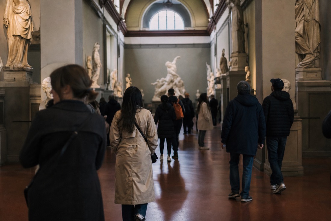 Visitors moving through the Hall of the Colossus at the Accademia Gallery in Florence with a large plaster sculpture group under a high ceiling