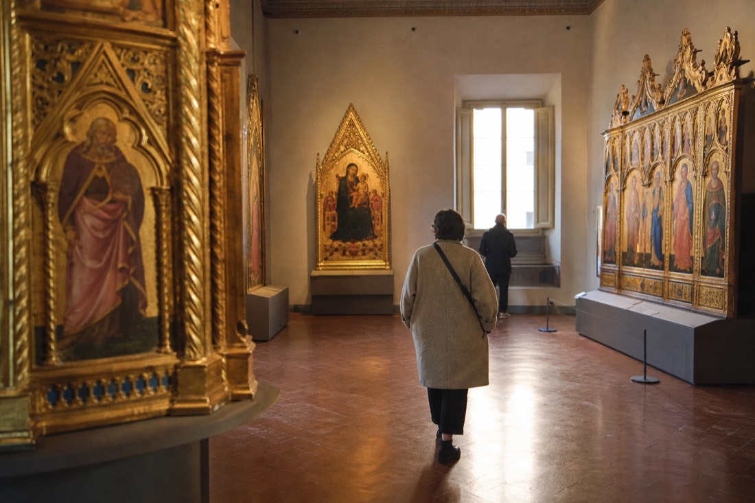 A quiet upstairs room of gold-ground medieval paintings at the Accademia Gallery in Florence with warm light on gilded altarpieces
