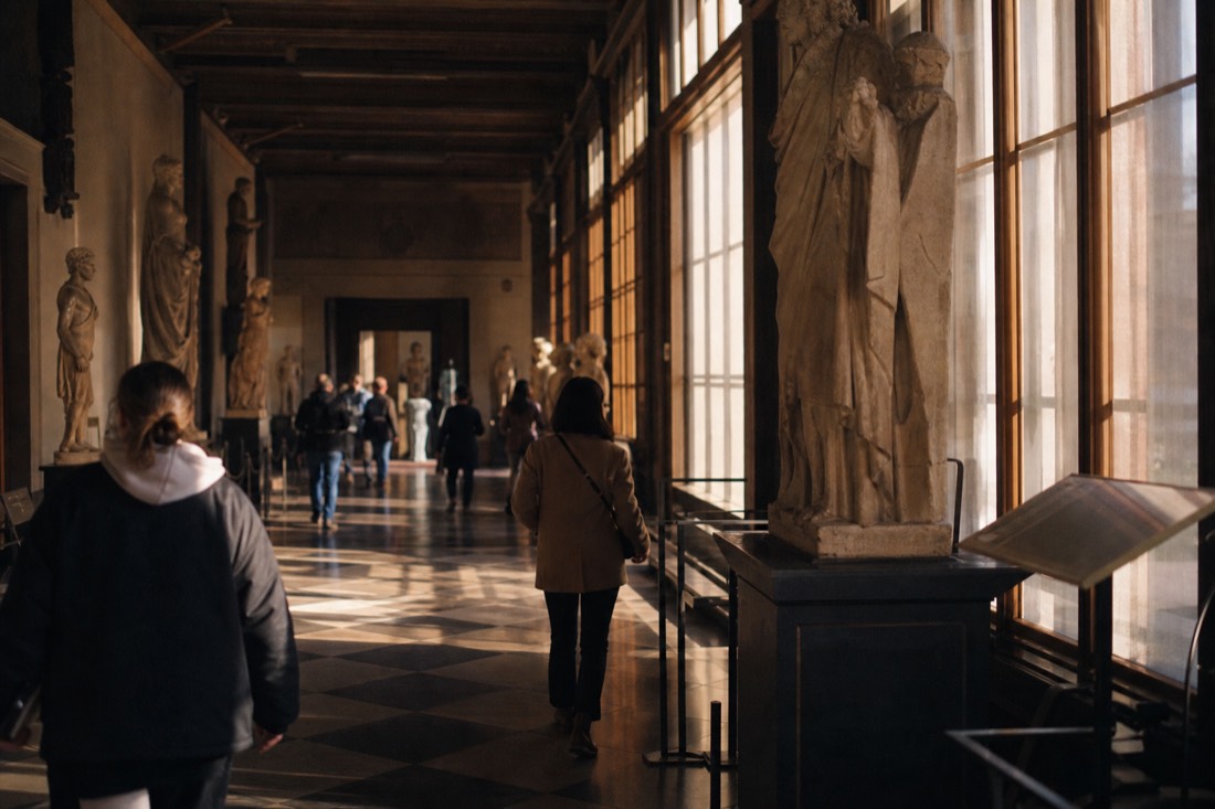 Warm late afternoon light falling through a tall museum gallery window onto a polished stone floor