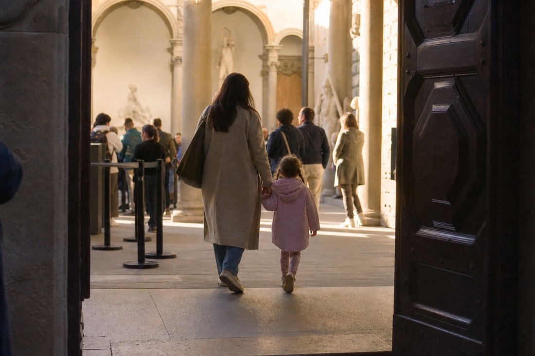 An adult holding a child's hand at the ticket entrance of the Accademia Gallery on Via Ricasoli in Florence