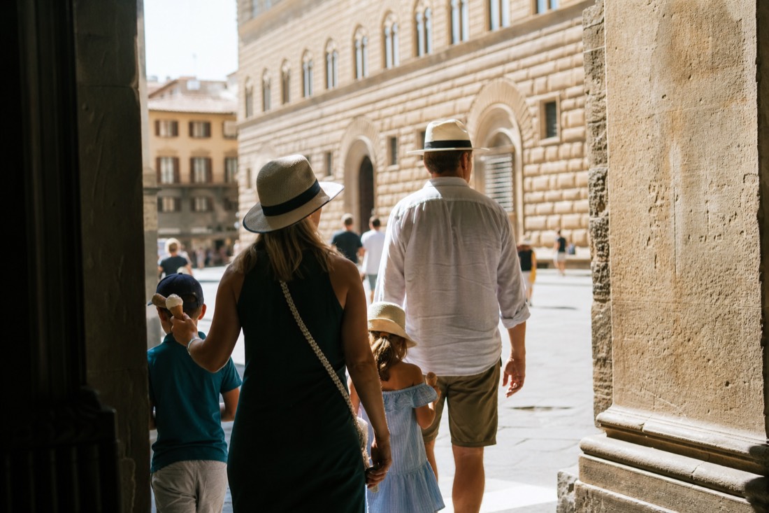 A family walking out of the Accademia Gallery into a sunlit Florence street in the late morning with gelato