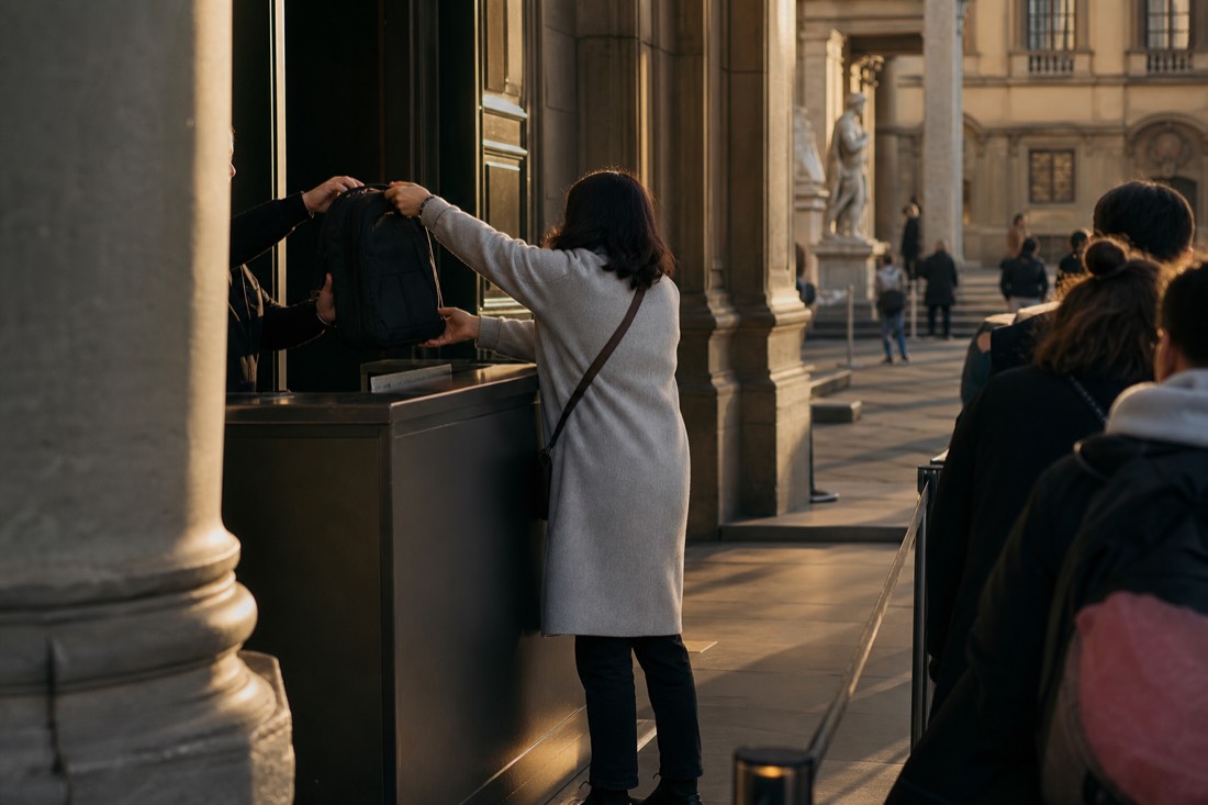A cloakroom counter near the Accademia entrance in Florence where a visitor hands over a backpack before entering the galleries