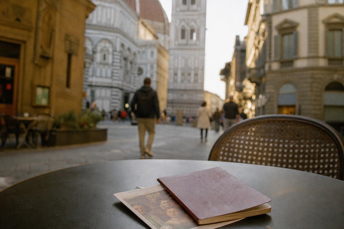 A passport and printed museum ticket resting on a cafe table with a Florence street blurred behind