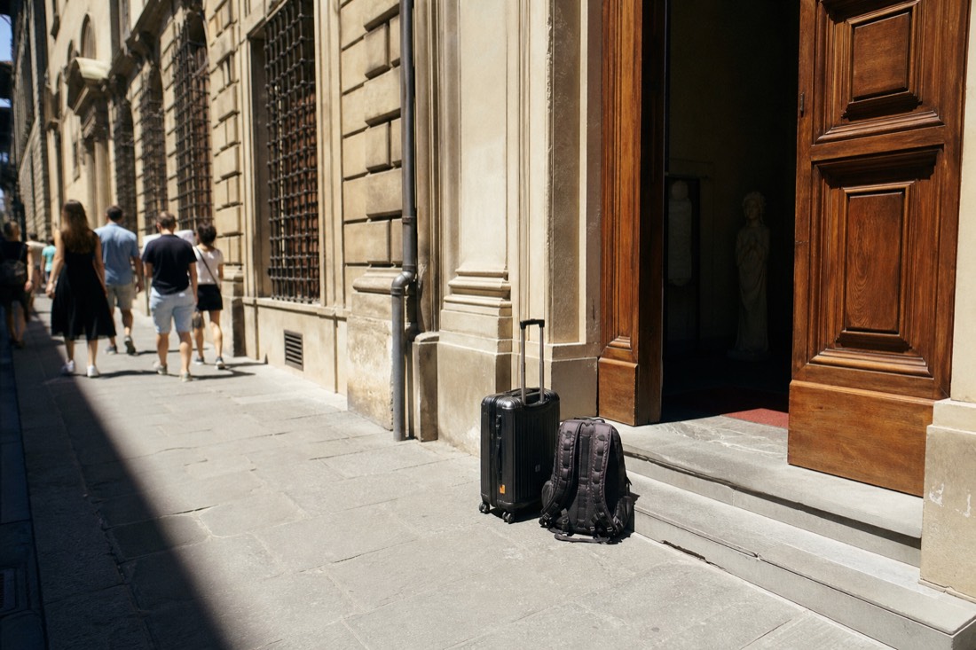 A wheeled suitcase and a large backpack set on the pavement outside the Accademia Gallery entrance on Via Ricasoli