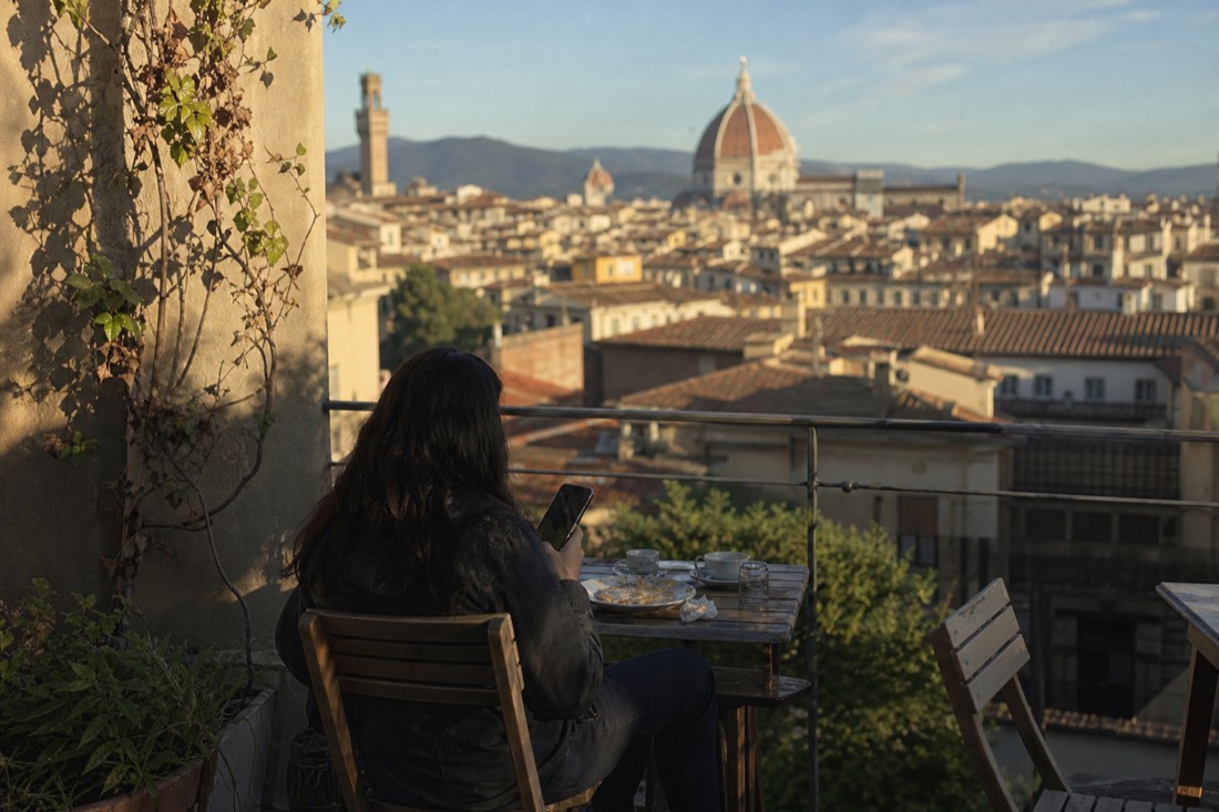 A traveller comparing prices on a phone at a Florence cafe with the Duomo dome visible over the rooftops