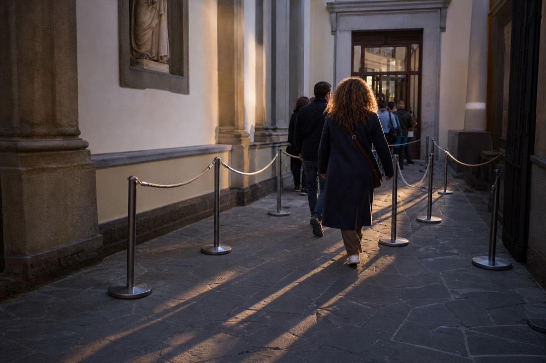 Metal stanchions and rope barriers set out in morning shade beside the Accademia Gallery ticket entrance