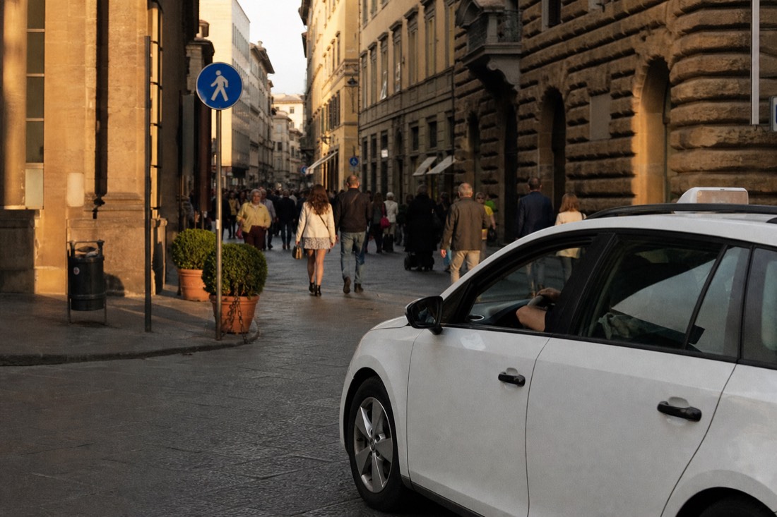 A white Florence taxi waiting at the edge of a limited-traffic zone on a narrow central street with pedestrian signage