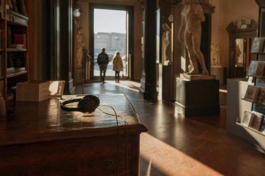 An audio guide headset resting on the wooden counter of the Accademia bookshop in Florence with gallery doorways beyond