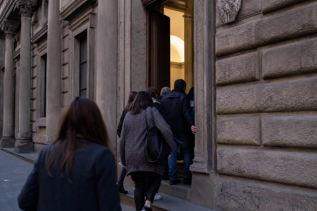 Early morning visitors entering the Accademia Gallery doorway on Via Ricasoli in Florence with soft light on the stone facade