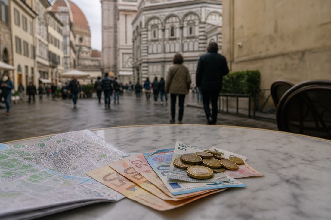 Euro banknotes and coins fanned across a worn marble cafe tabletop beside a folded Florence street map