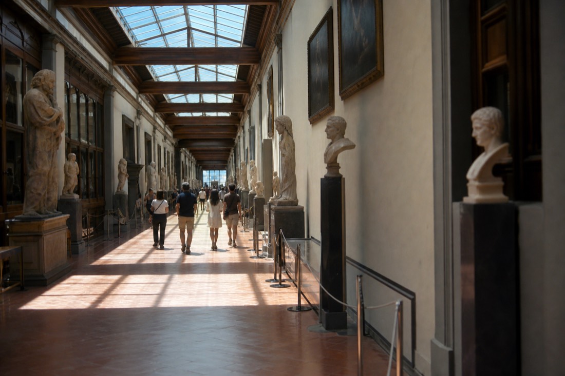 The long skylit sculpture corridor of the Accademia Gallery in Florence seen from its far end with statues in soft morning light