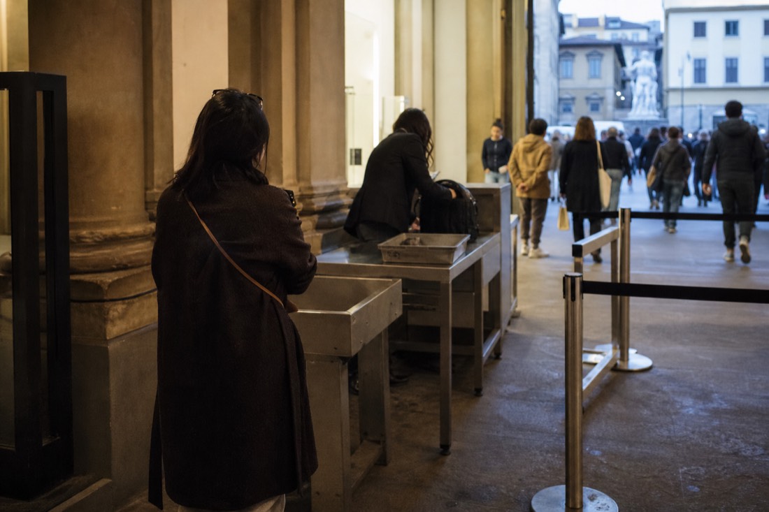 A security desk at a Florence museum entrance where a small bag is allowed through and a larger backpack is set aside