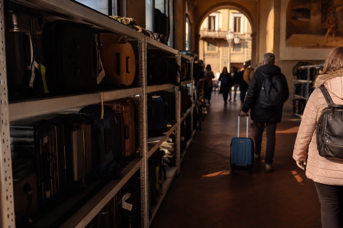 Rows of stored suitcases and backpacks on shelves at a left-luggage deposit near a Florence train station