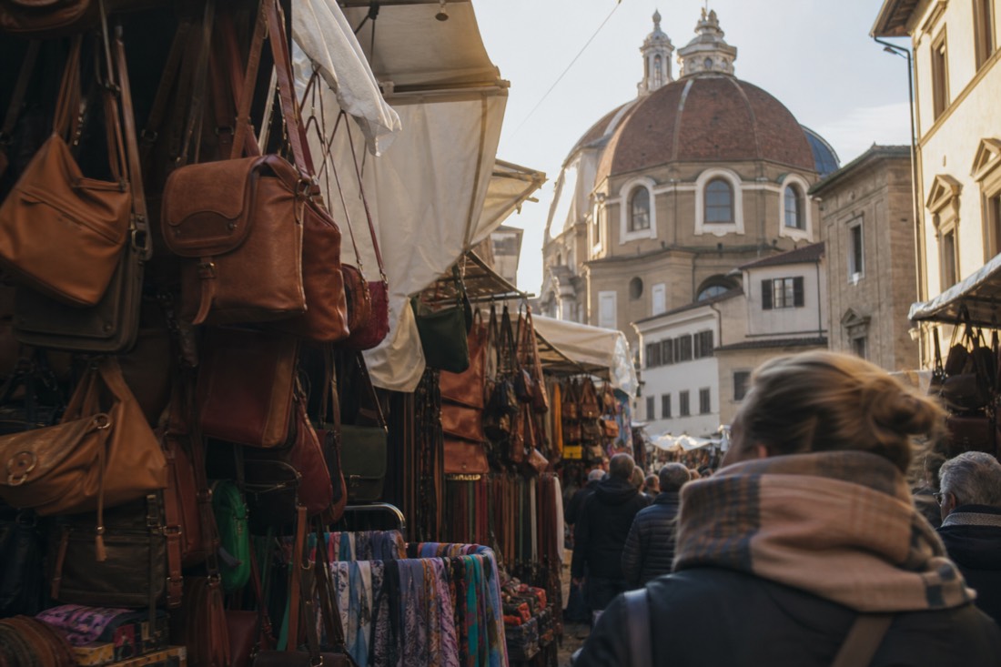 Leather bags and scarves on San Lorenzo market stalls with the dome of the Medici chapels rising behind