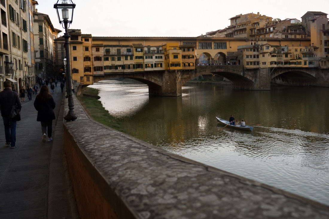 Ponte Vecchio glowing in late afternoon light over the Arno with a single rowing boat on the green water