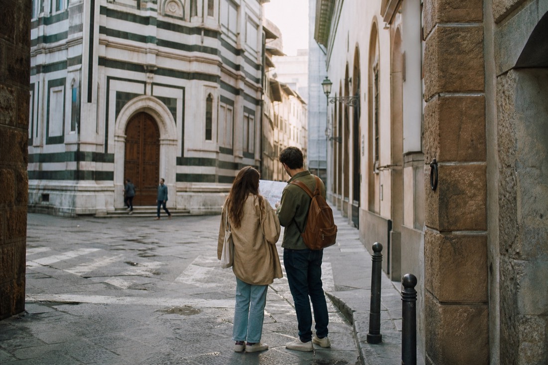 A couple pausing on a Florence street corner with a paper map deciding between two directions in warm afternoon light