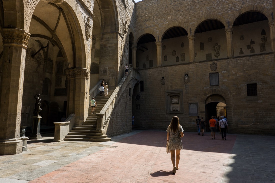 The stone courtyard and open staircase of the Museo del Bargello in Florence under sharp afternoon light