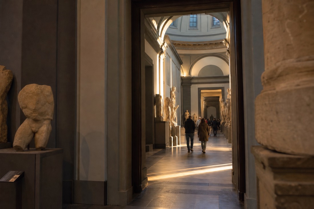 A sunlit line of gallery doorways leading from the Hall of the Colossus toward the domed tribune in the Accademia Gallery in Florence
