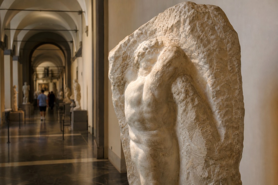 A single half-carved Michelangelo Prisoner lit from above in a quiet stretch of the Accademia corridor in Florence