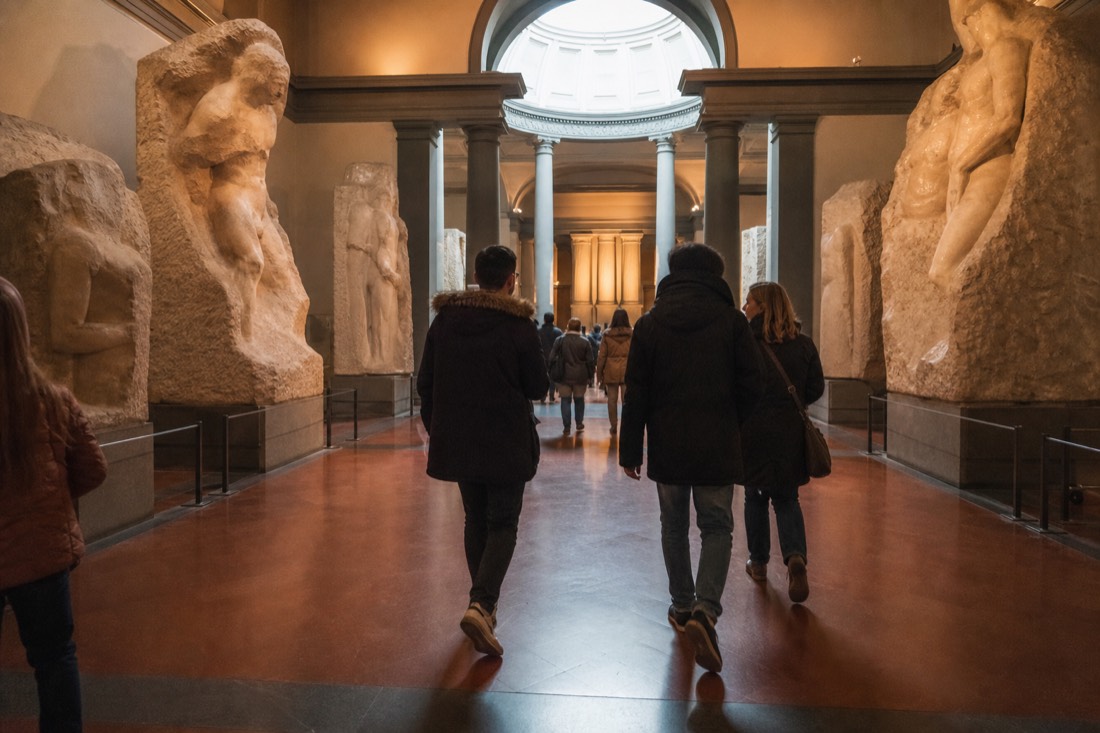 Visitors walking the Hall of the Prisoners inside the Accademia Gallery Florence toward the Tribuna